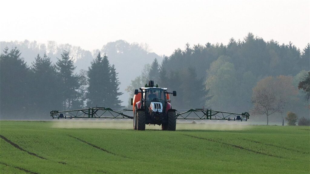 A tractor spraying chemicals on a field against a backdrop of trees.